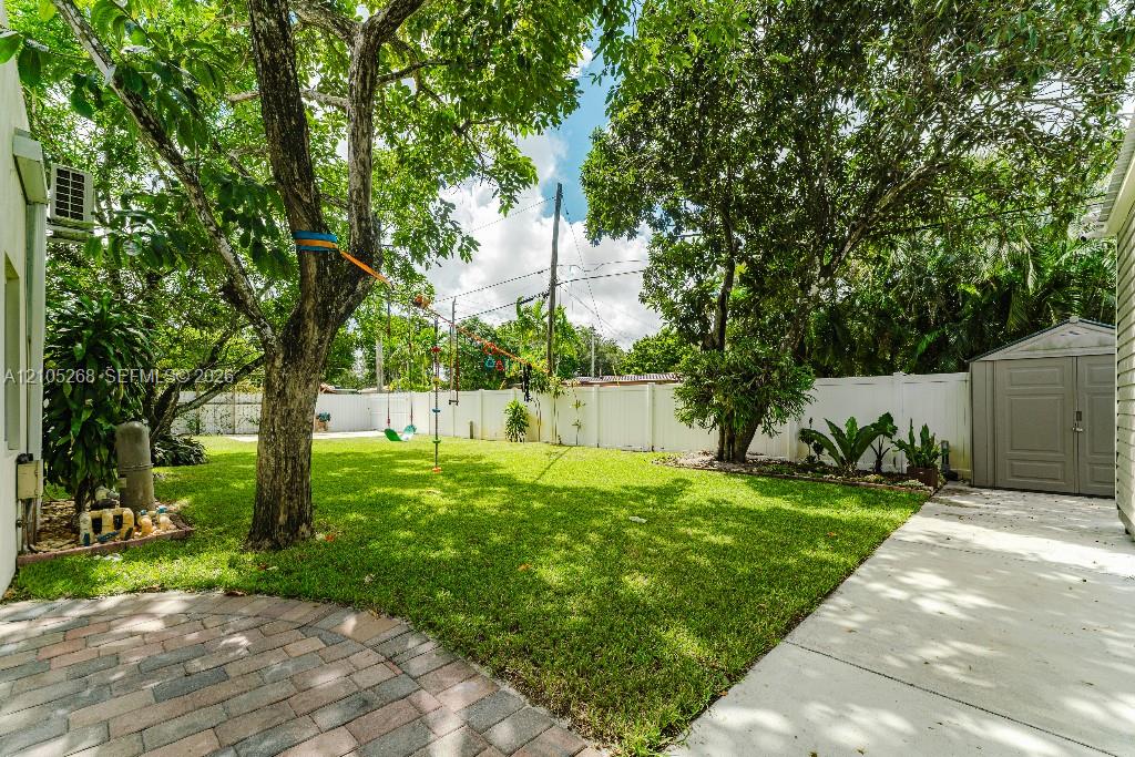 Manicured lawn, mature trees, white privacy fencing, paved patio area, and a storage shed