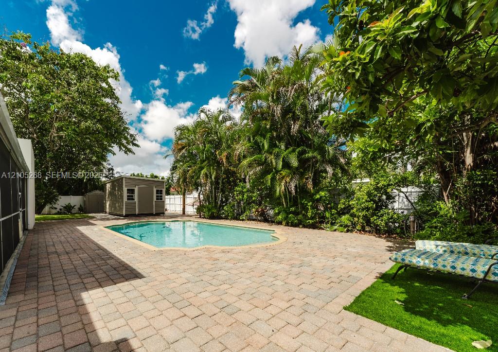 Paved patio with an in-ground pool, surrounded by mature trees and lush landscaping