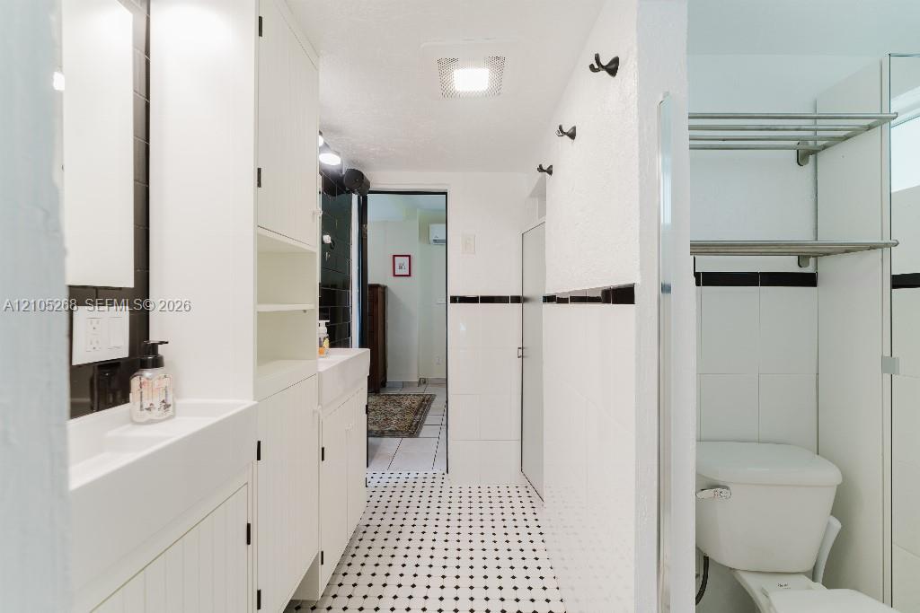 Black and white mosaic tile flooring, built-in white cabinetry, integrated sink, white tiled walls with black accent banding, and a white toilet