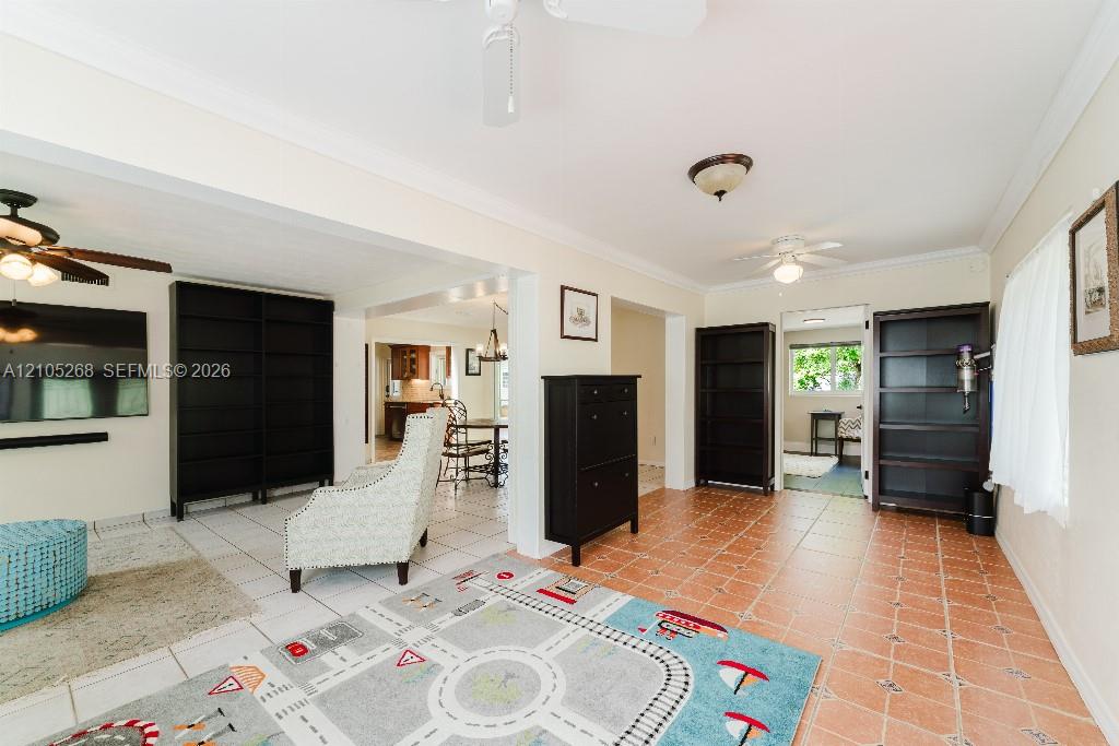 Expansive room featuring light tile flooring, crown molding, and two ceiling fans