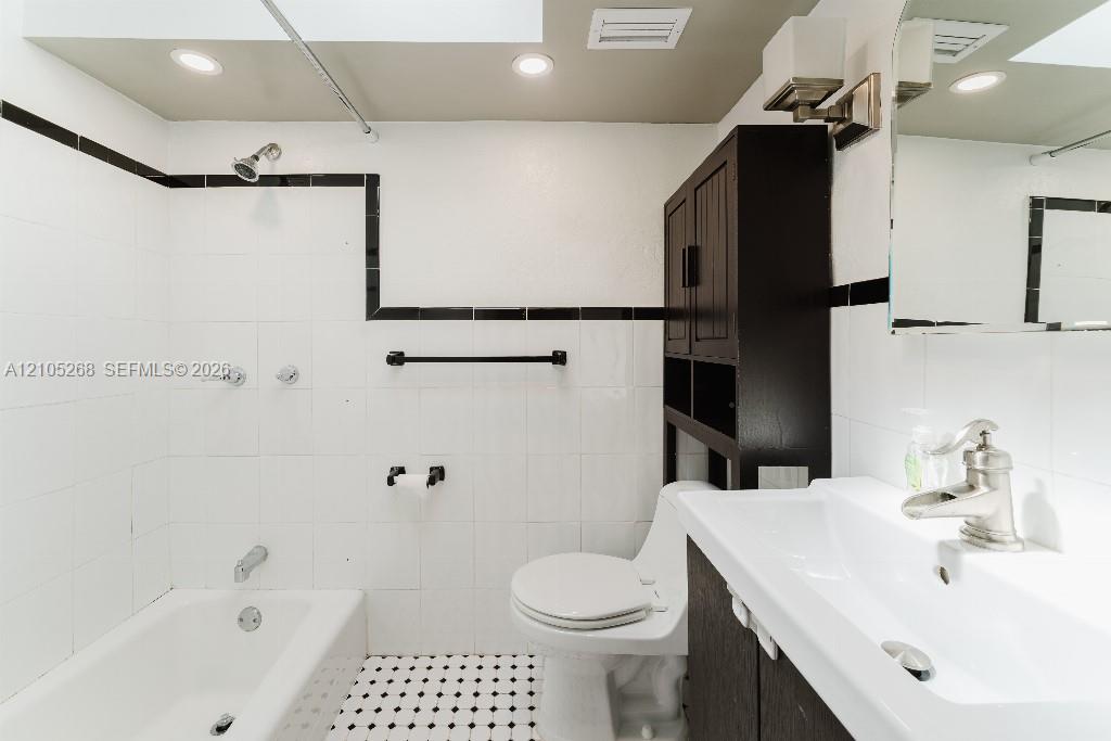 White subway tile with black trim, recessed lighting, black and white mosaic floor tile, white vanity with integrated sink, and dark wood-finish cabinet