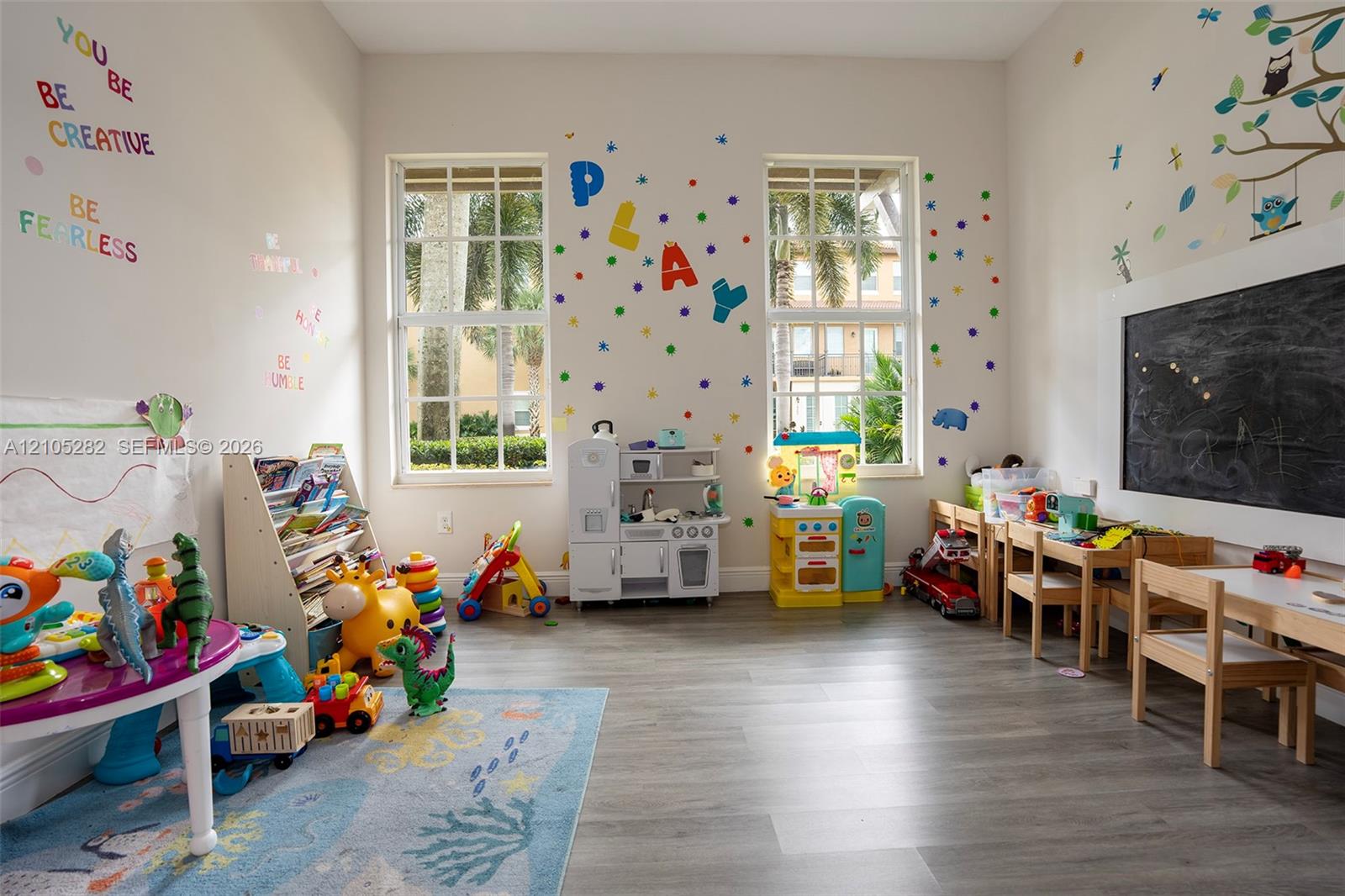 Room featuring high ceilings, wood-finish flooring, two large multi-pane windows, and a built-in chalkboard