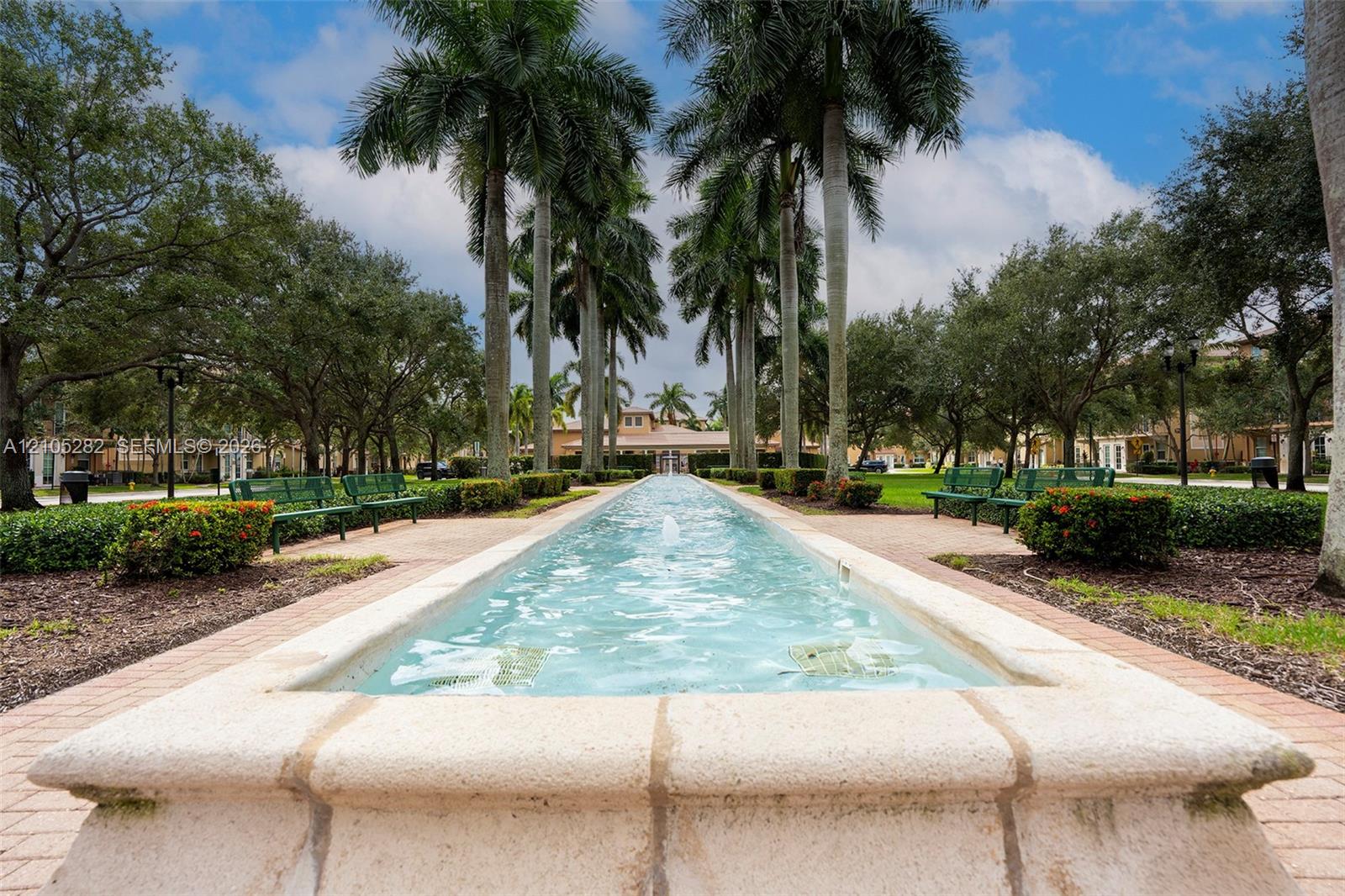 Linear water feature with stone coping, lined by mature palm trees, manicured hedges, and paver pathways