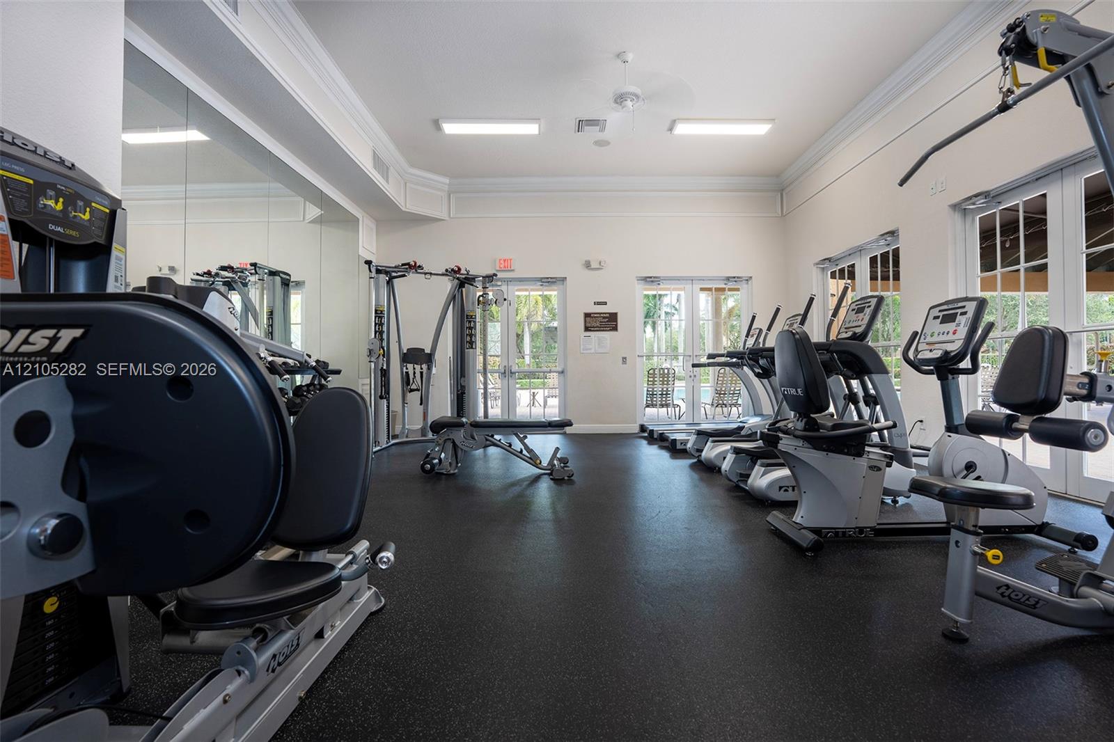 Fitness center featuring rubber flooring, floor-to-ceiling mirrored walls, crown molding, and dual glass-paned double doors
