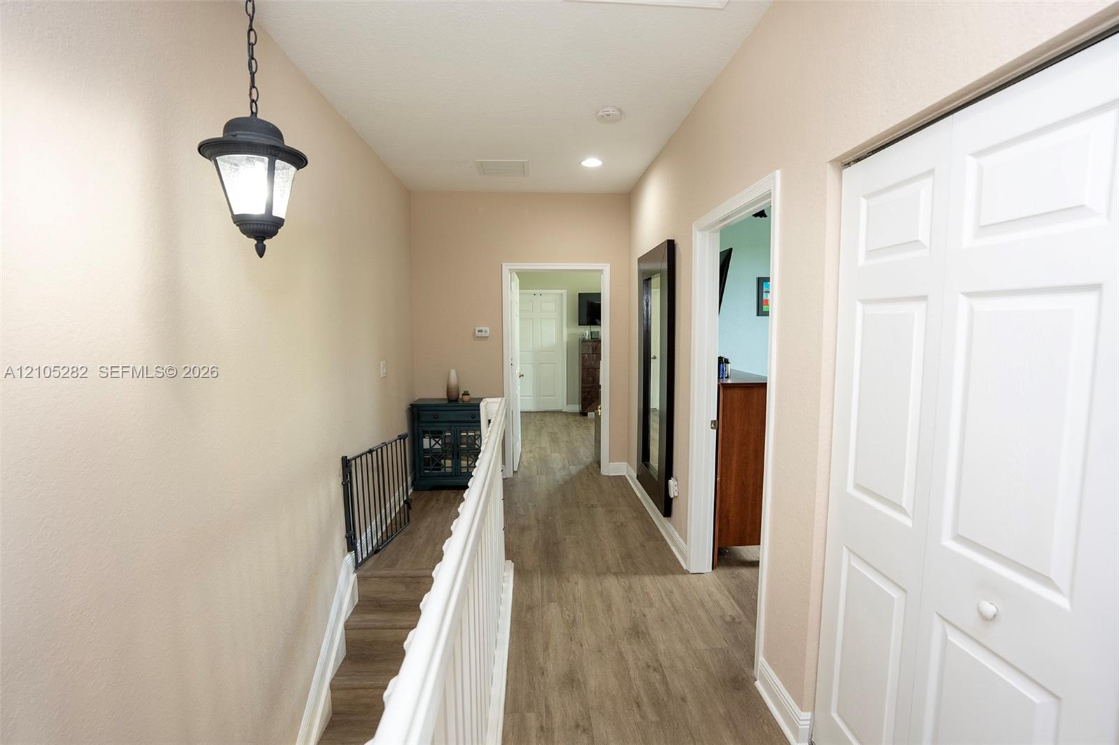 Hallway featuring wood-finish flooring, a hanging lantern-style light fixture, white wood-slat railing, and bifold closet doors