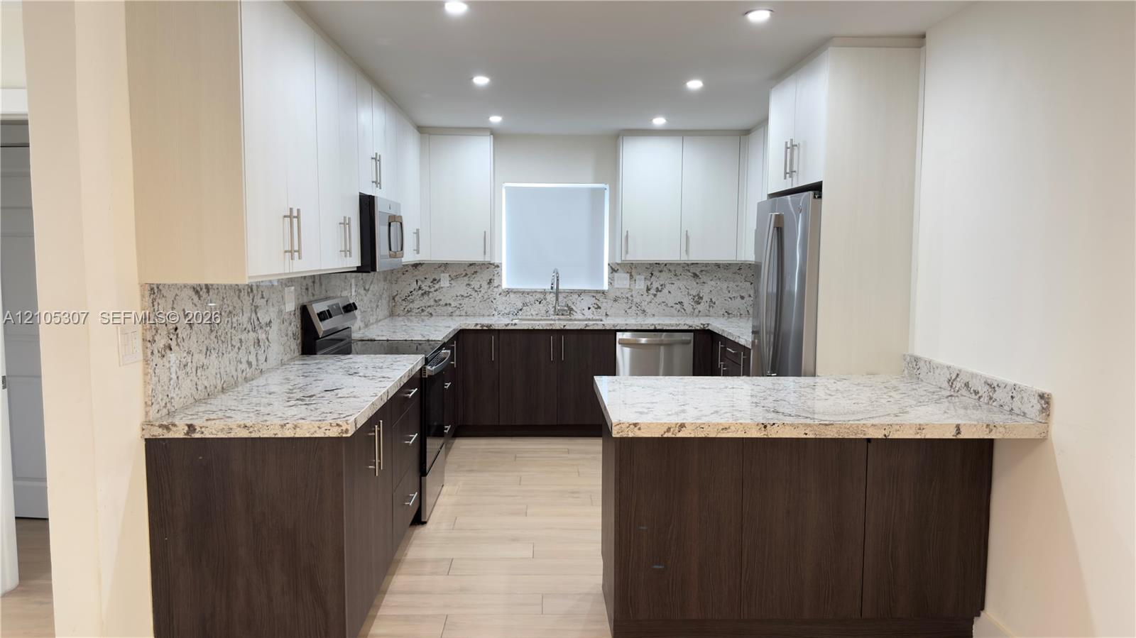 Kitchen featuring two-tone cabinetry, stone-finish countertops, stainless steel appliances, recessed ceiling lighting, and wood-finish flooring Kitchen featuring two-tone cabinetry, stone-finish countertops, stainless steel appliances, recessed ceiling lighting, and wood-finish flooring