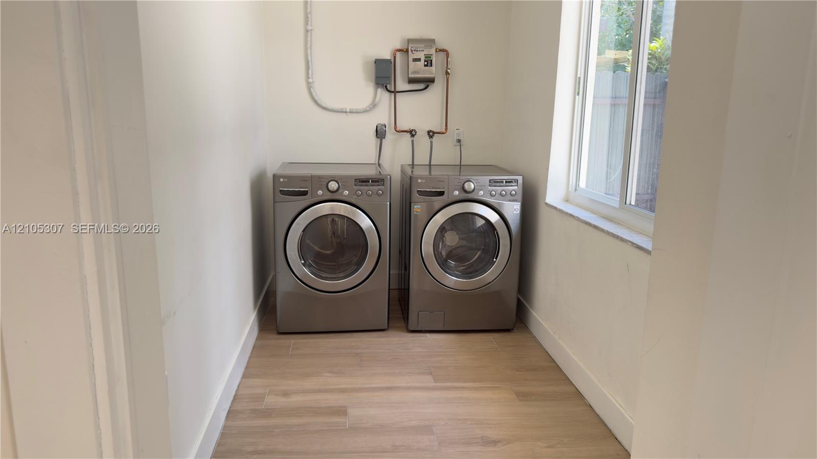 Dedicated laundry space featuring wood-finish flooring and a single-hung window Dedicated laundry space featuring wood-finish flooring and a single-hung window