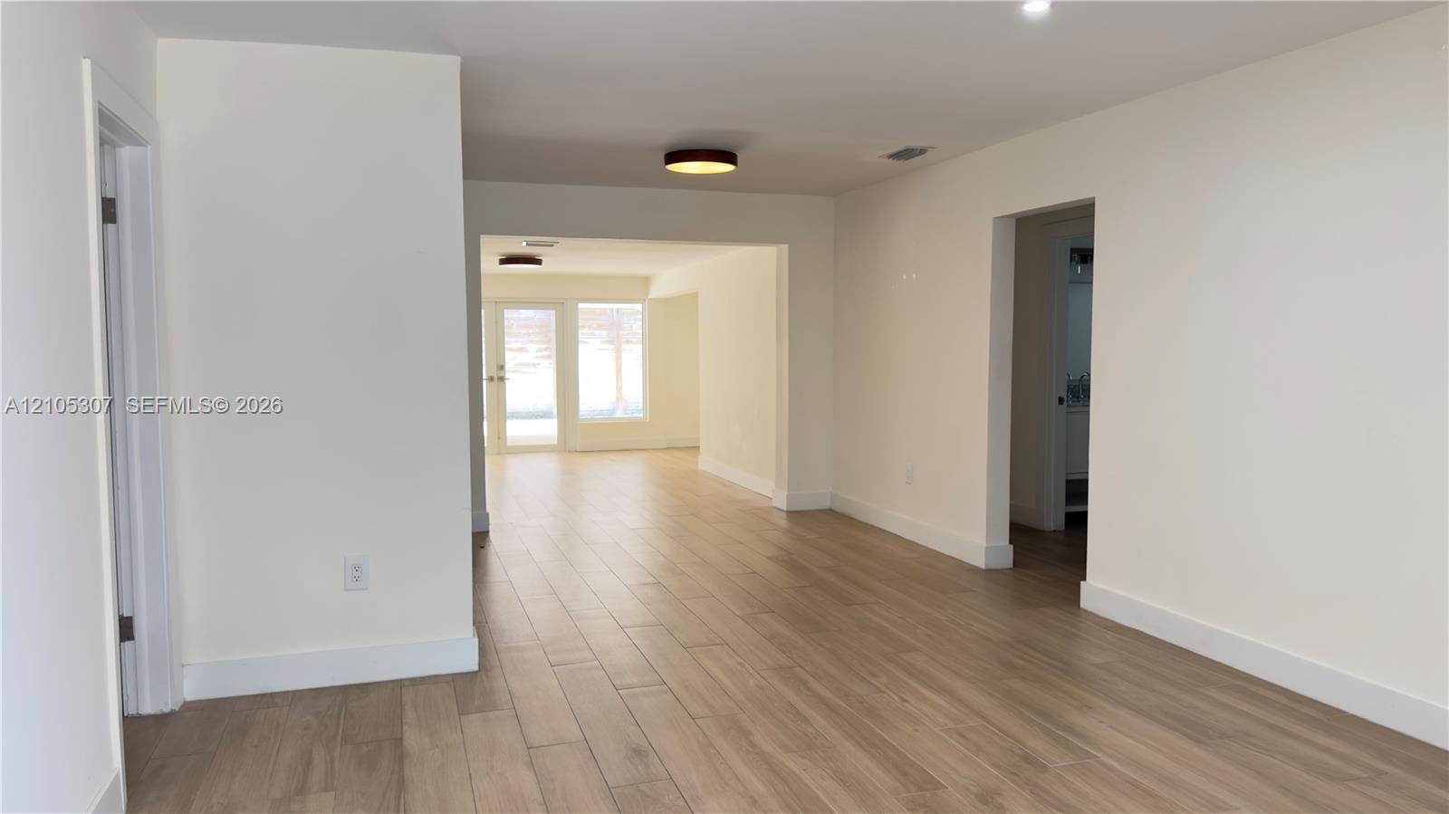 Interior space featuring wood-finish flooring, crisp white walls, flush-mount ceiling lighting, and multi-pane glass doors Interior space featuring wood-finish flooring, crisp white walls, flush-mount ceiling lighting, and multi-pane glass doors
