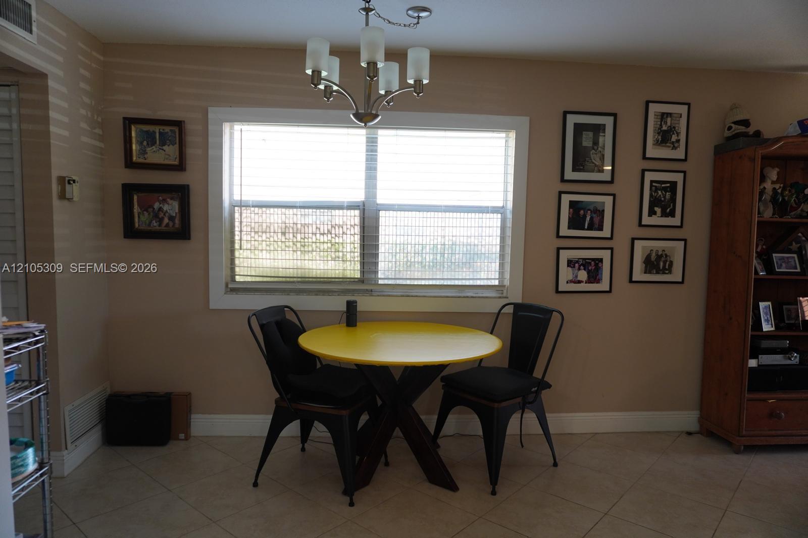 Interior area featuring large window with wide casing, tile flooring, and five-arm chandelier light fixture