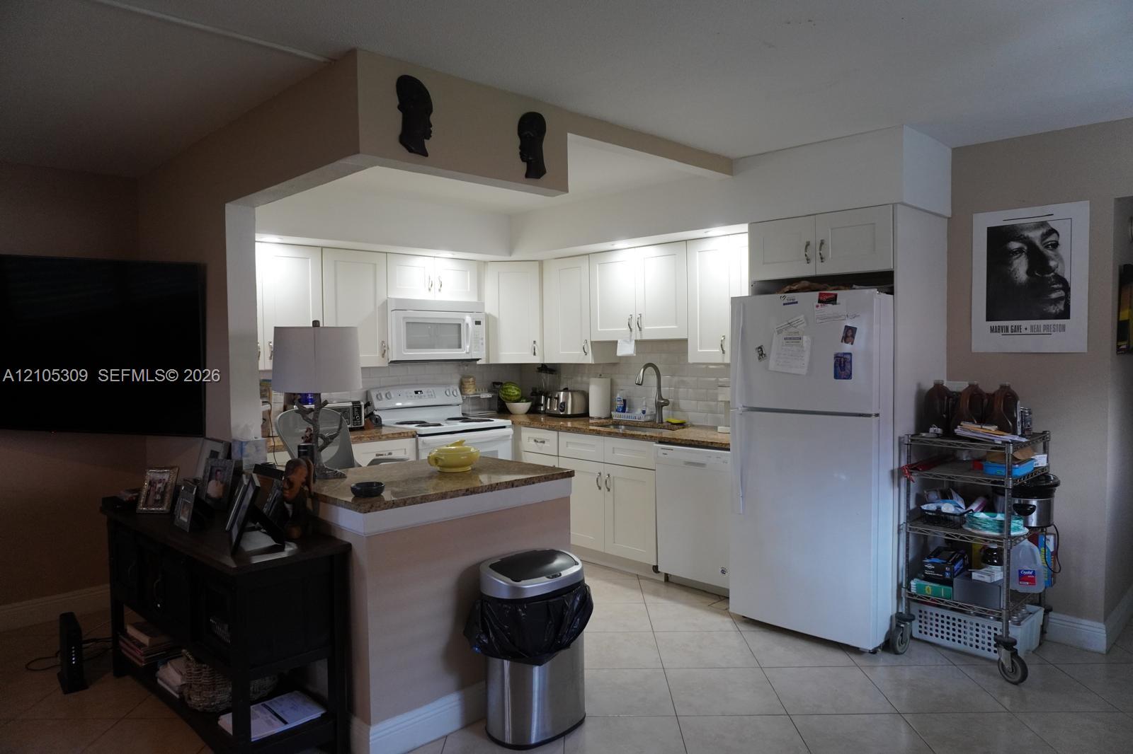 Kitchen featuring white shaker-style cabinetry, stone-finish countertops, tiled backsplash, and built-in appliances including a dishwasher and microwave Kitchen featuring white shaker-style cabinetry, stone-finish countertops, tiled backsplash, and built-in appliances including a dishwasher and microwave