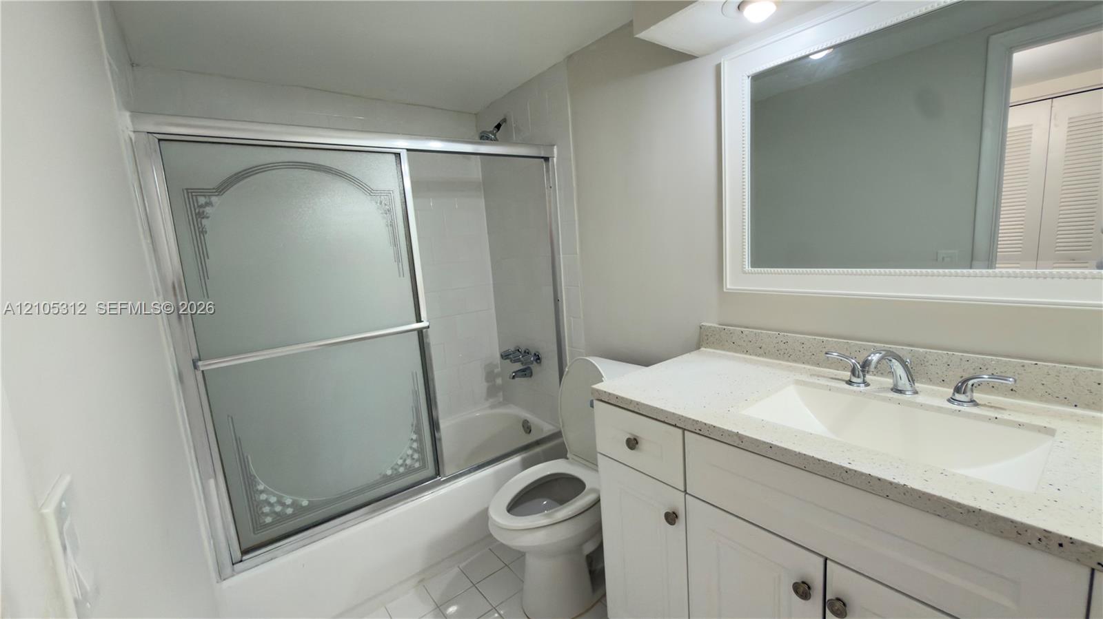 Bathroom featuring a white vanity cabinet with a speckled countertop, integrated sink with a chrome faucet, large framed wall mirror, and a shower-tub combination with sliding etched-glass doors