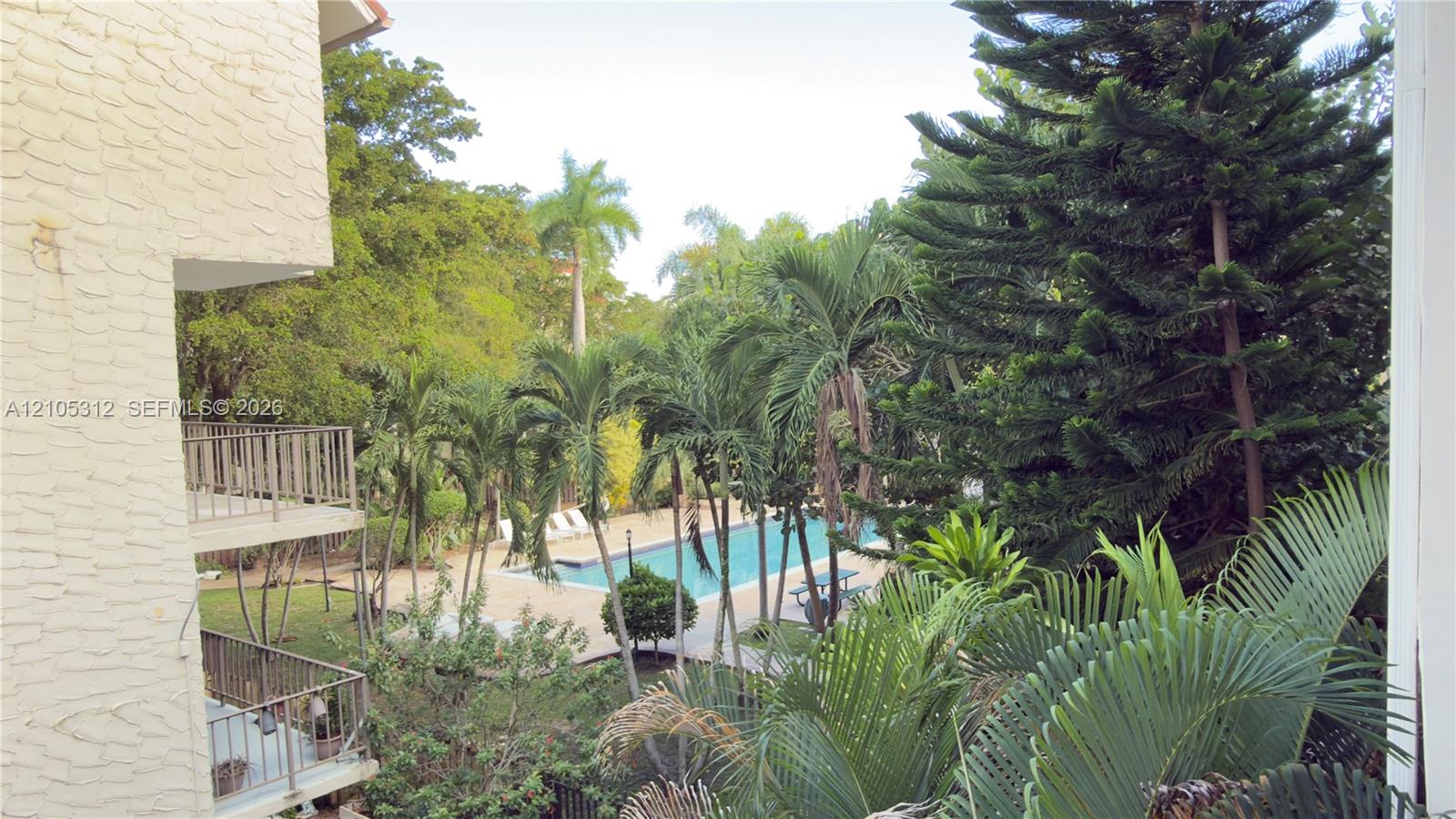 Outdoor space featuring an in-ground swimming pool, multi-level metal-railed balconies, and mature landscaping including palm and evergreen trees
