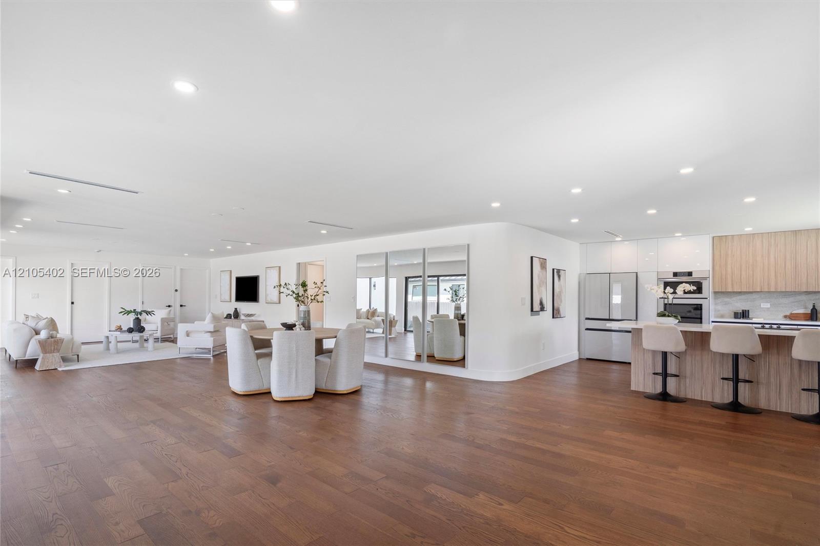 Open-concept interior featuring wood-finish flooring, recessed lighting, a built-in mirrored wall, and a kitchen equipped with wood-finish cabinetry and a tiered island
