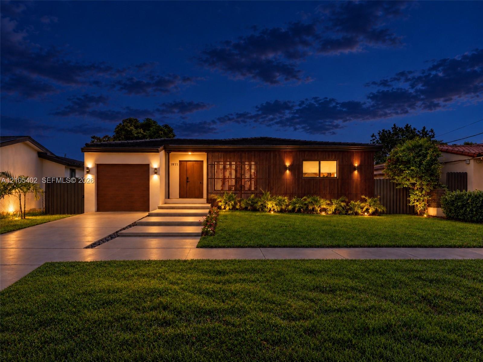 Modern single-story exterior featuring a wood-panel faade, integrated wall sconce lighting, solid wood front door, horizontal-slat garage door, and concrete entry steps
