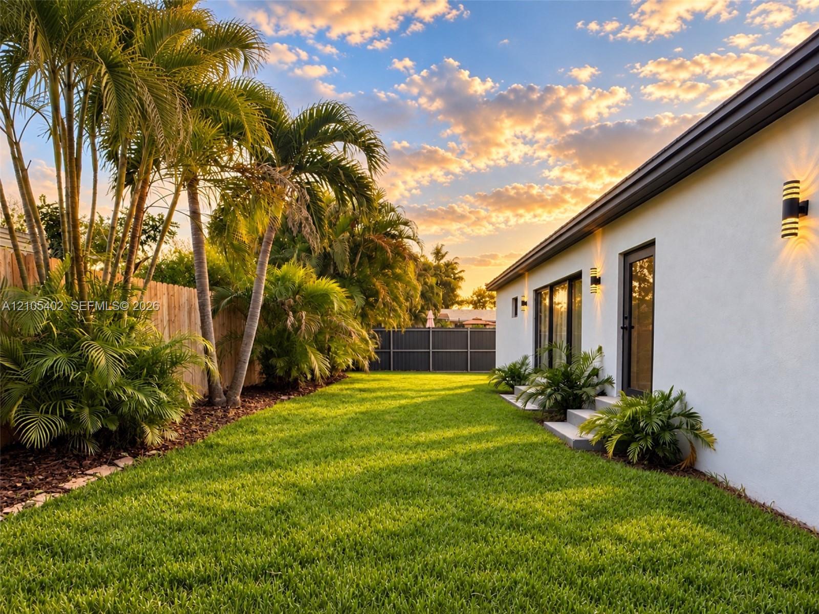 Expansive backyard featuring a manicured lawn, mature palm trees, exterior wall-mounted lighting, and privacy fencing