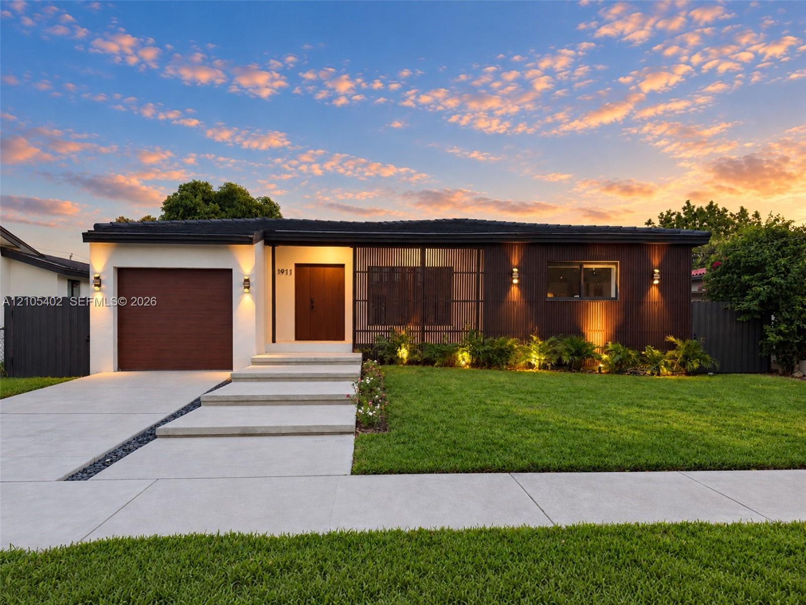 Single-story residence featuring a mid-century modern aesthetic, wood-paneled exterior accents, a concrete driveway with stone drainage detail, a stepped concrete entryway, and wall-mounted exterior lighting