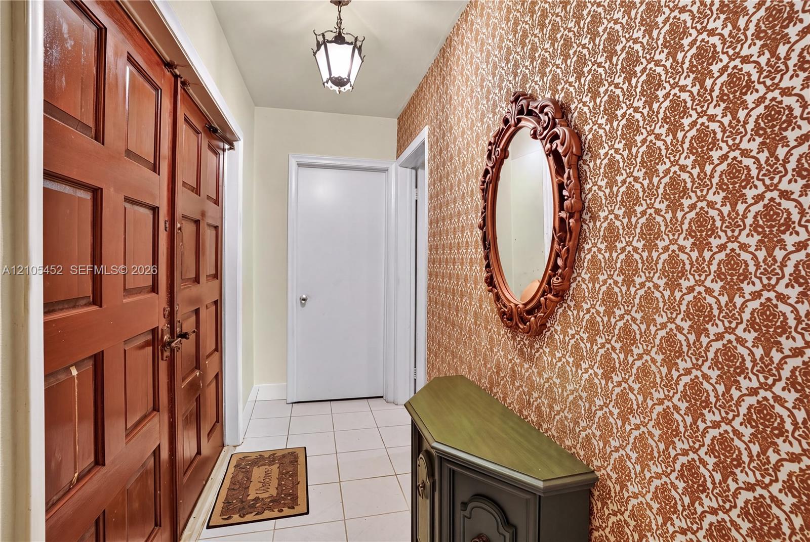 Entryway featuring double wood-paneled doors, ceramic tile flooring, and patterned wallcovering