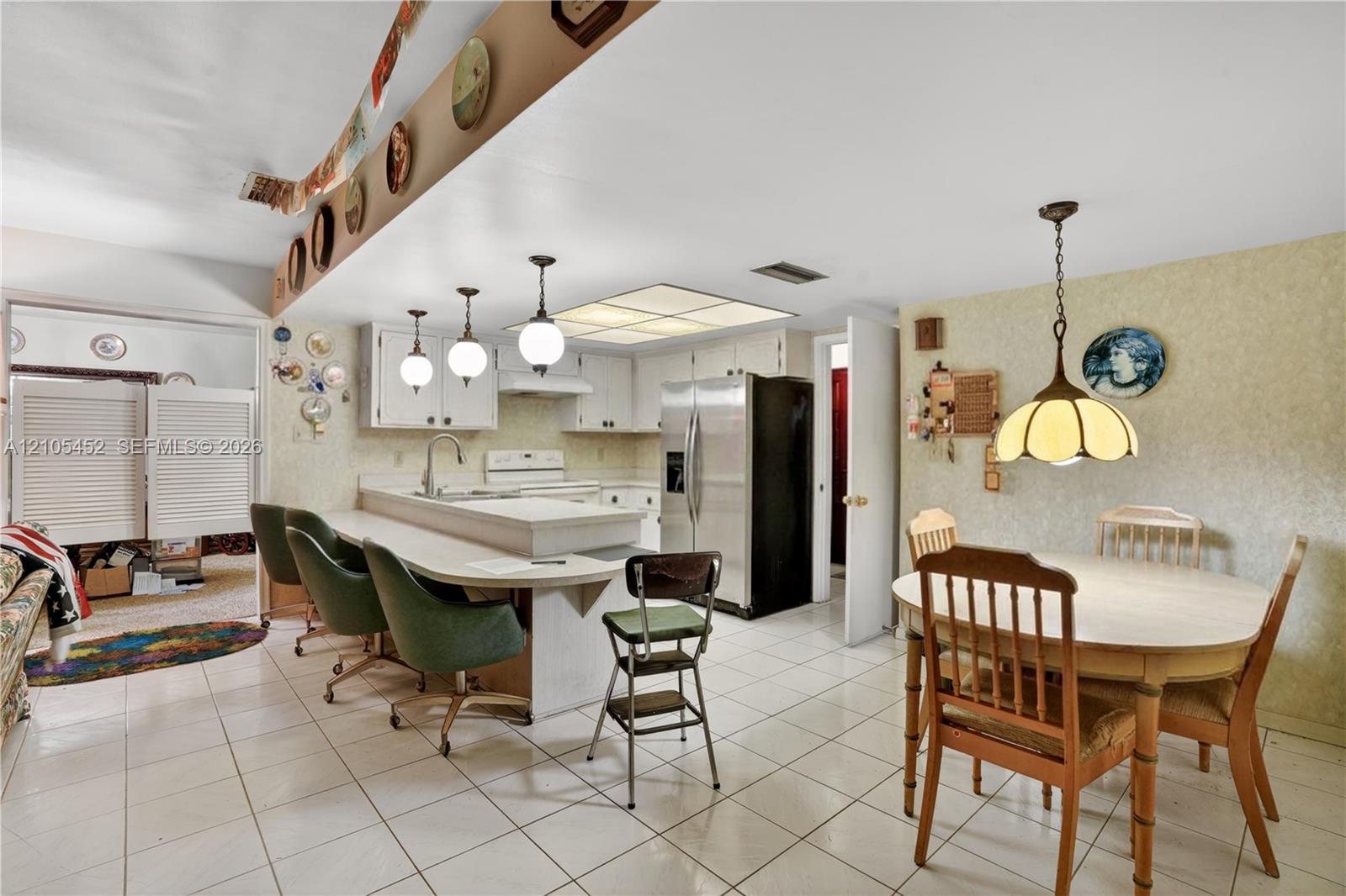 Kitchen featuring a tiered peninsula with a breakfast bar, white cabinetry, tile flooring, recessed ceiling lighting, and three pendant lights