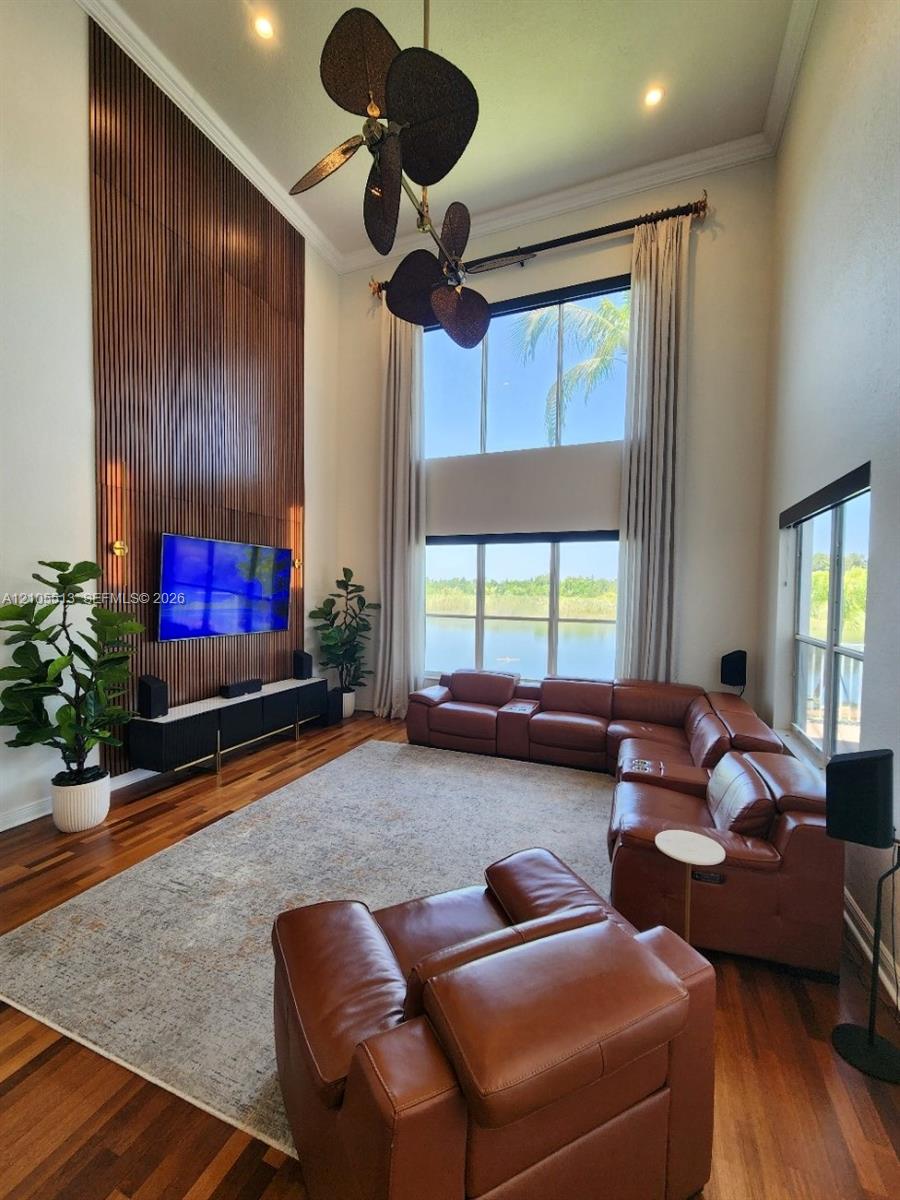 Hardwood flooring, 20ft high ceilings with crown molding & custom ceiling fan, natural light from expansive windows, and a built-in wood-slat media panel feature with integrated lighting sconces
