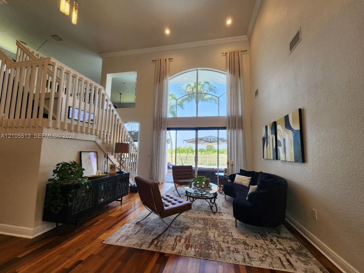 Hardwood flooring, soaring 20ft ceilings, large arched window, sliding glass doors, and a staircase with white balusters