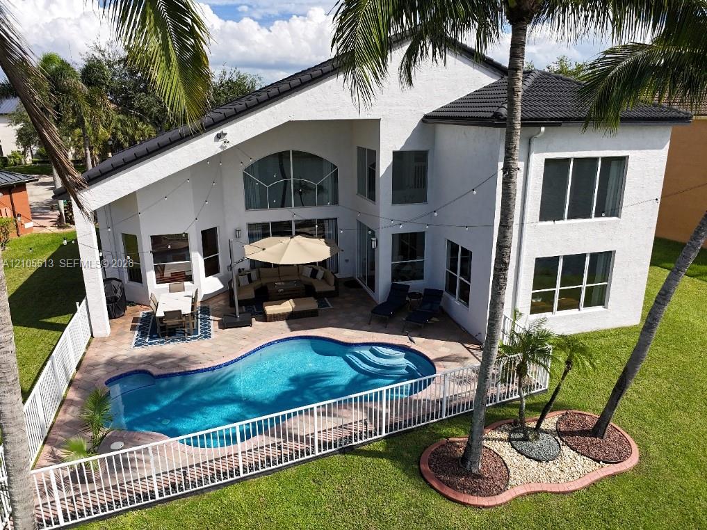 White stucco exterior with a dark tile roof, a private fenced pool, and a paver patio