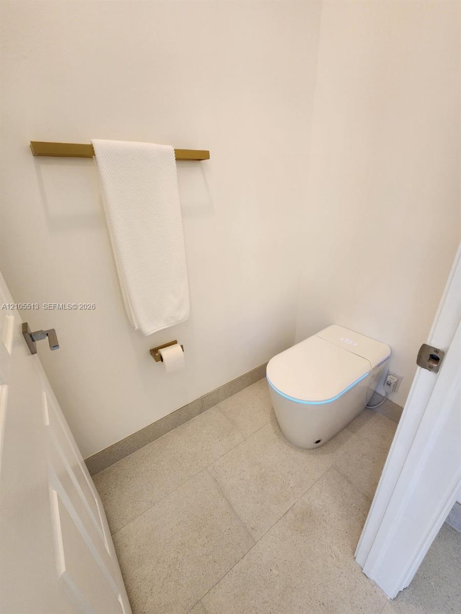 White walls with a modern smart toilet, porcelain flooring, and matching gold-finish fixtures