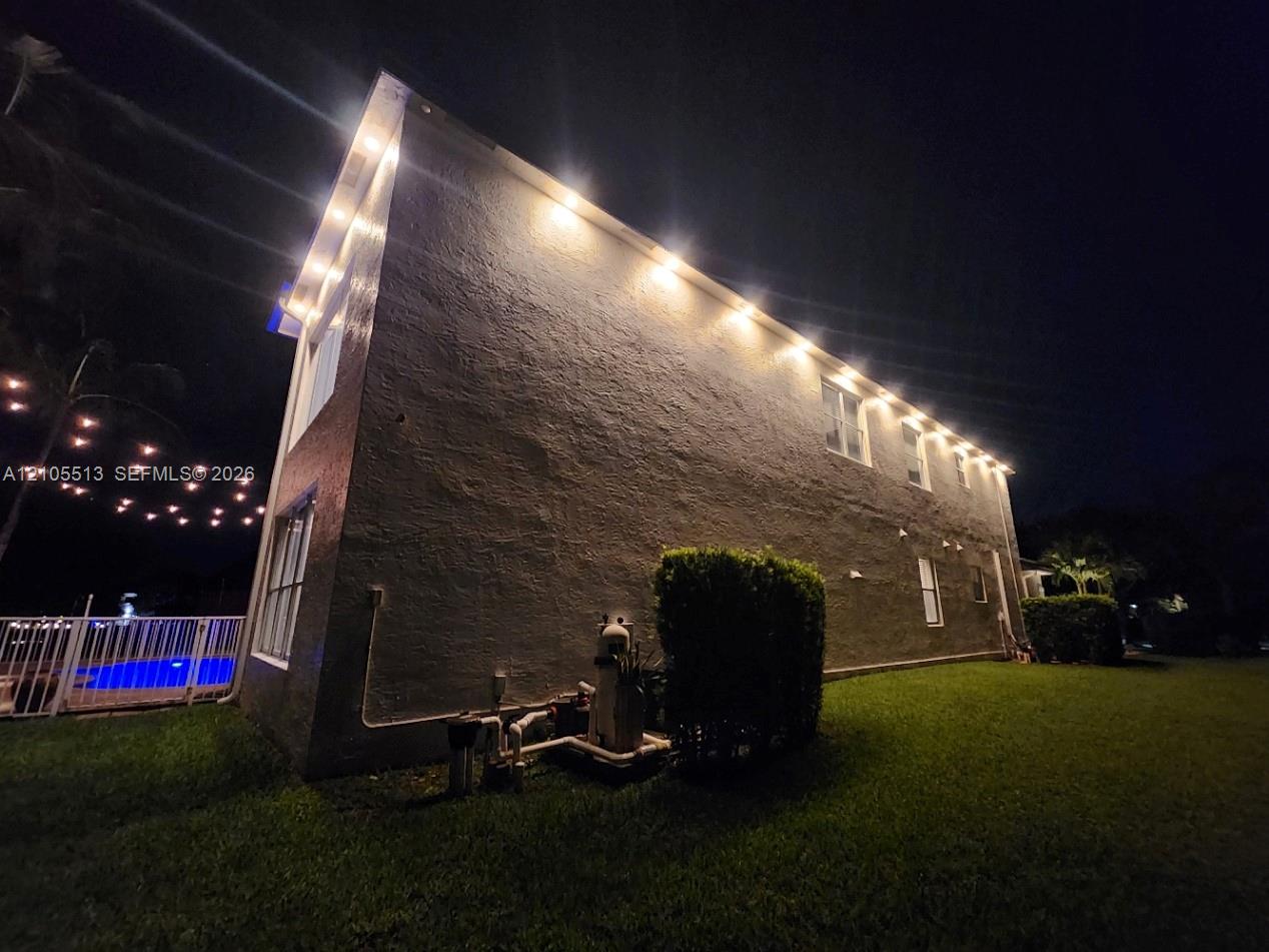 Night view of side with automated security down lighting, low voltage string lights & multi-colored pool light