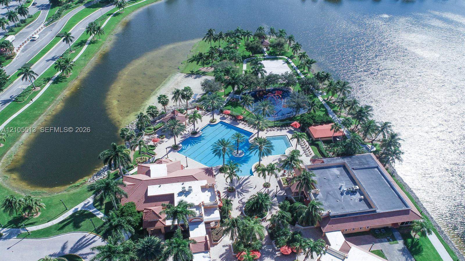 Waterfront community amenities featuring a large swimming pool, paved walking paths, manicured landscaping, and mature palm trees