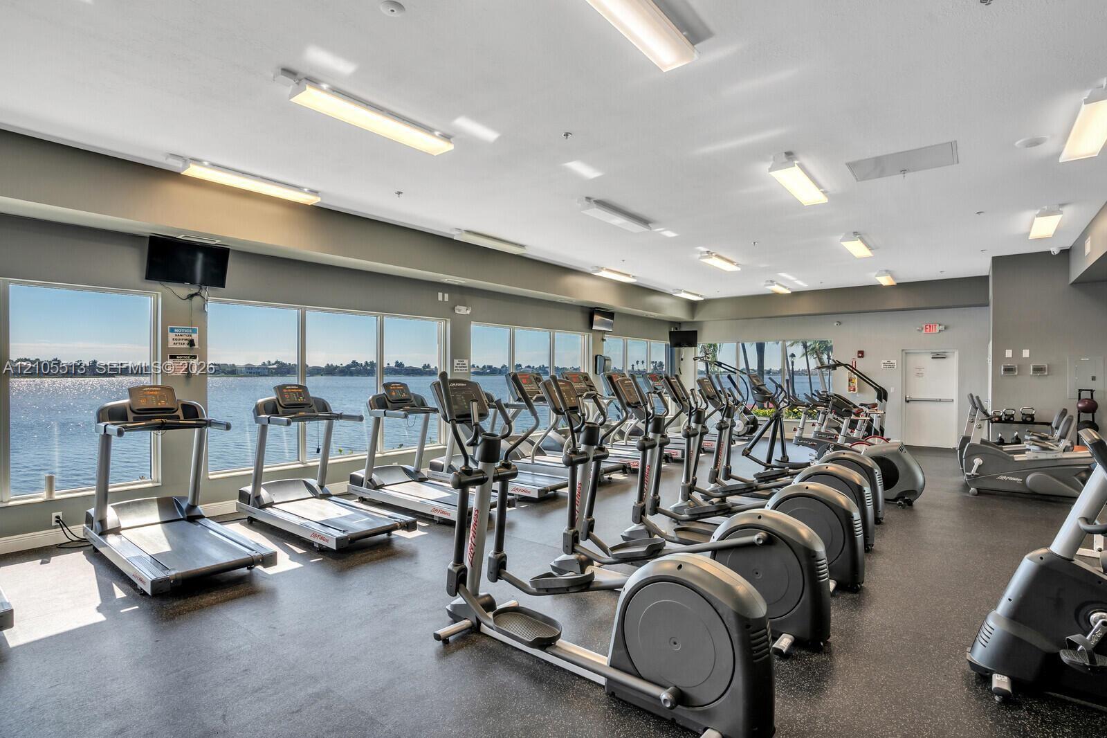 Fitness center featuring full-length floor-to-ceiling windows, water frontage, rubberized flooring, and recessed linear lighting