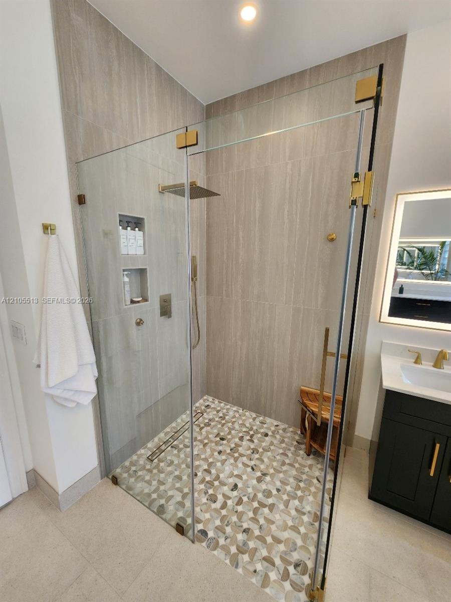 Glass-enclosed shower with custom marble tiled flooring, a built-in shower niche, and a rain shower head