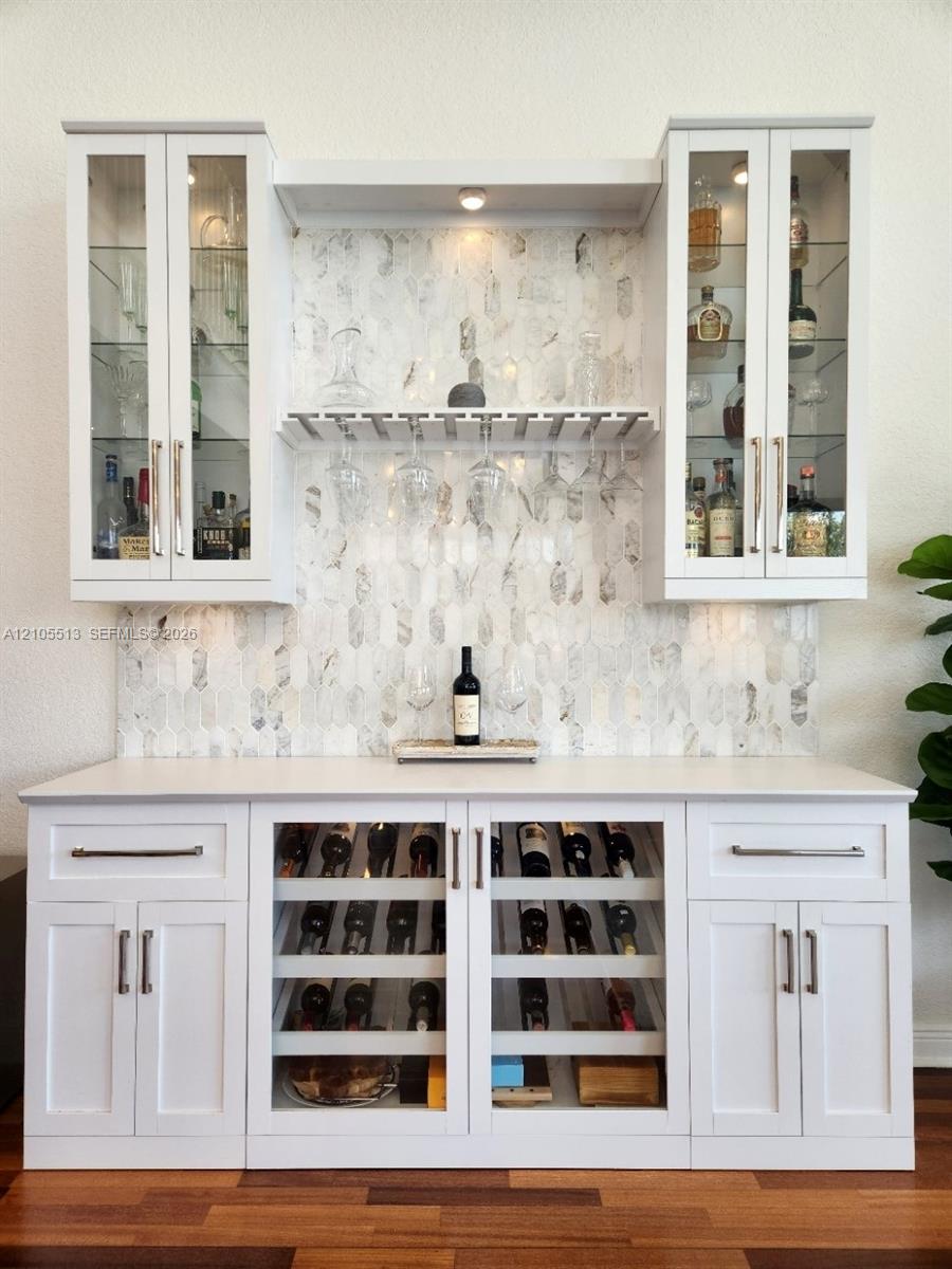Custom built-in bar featuring upper glass-front cabinetry, a marble backsplash, under-cabinet lighting, and integrated wine storage with glass doors