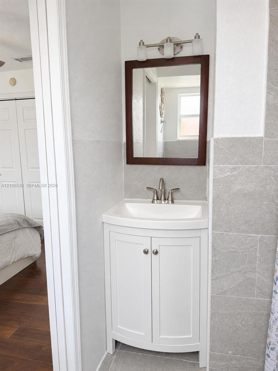 Corner vanity with white cabinetry, light gray tile flooring, and a rectangular framed mirror