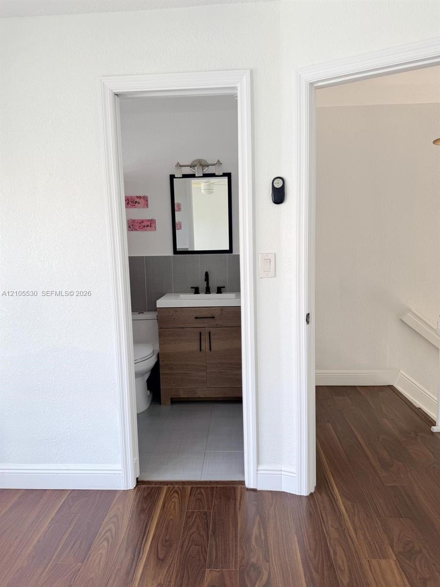 Wood-finish flooring throughout, with a bathroom featuring a wood-finish vanity, a wall-mounted mirror, and tile flooring