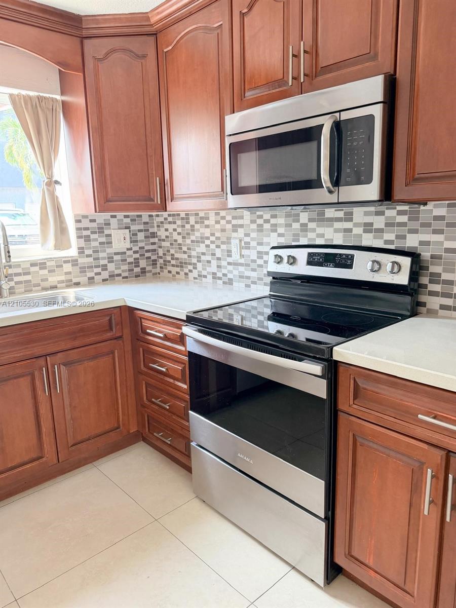 Contemporary kitchen featuring wood cabinetry, stainless steel appliances, a mosaic tile backsplash, and light-toned countertops