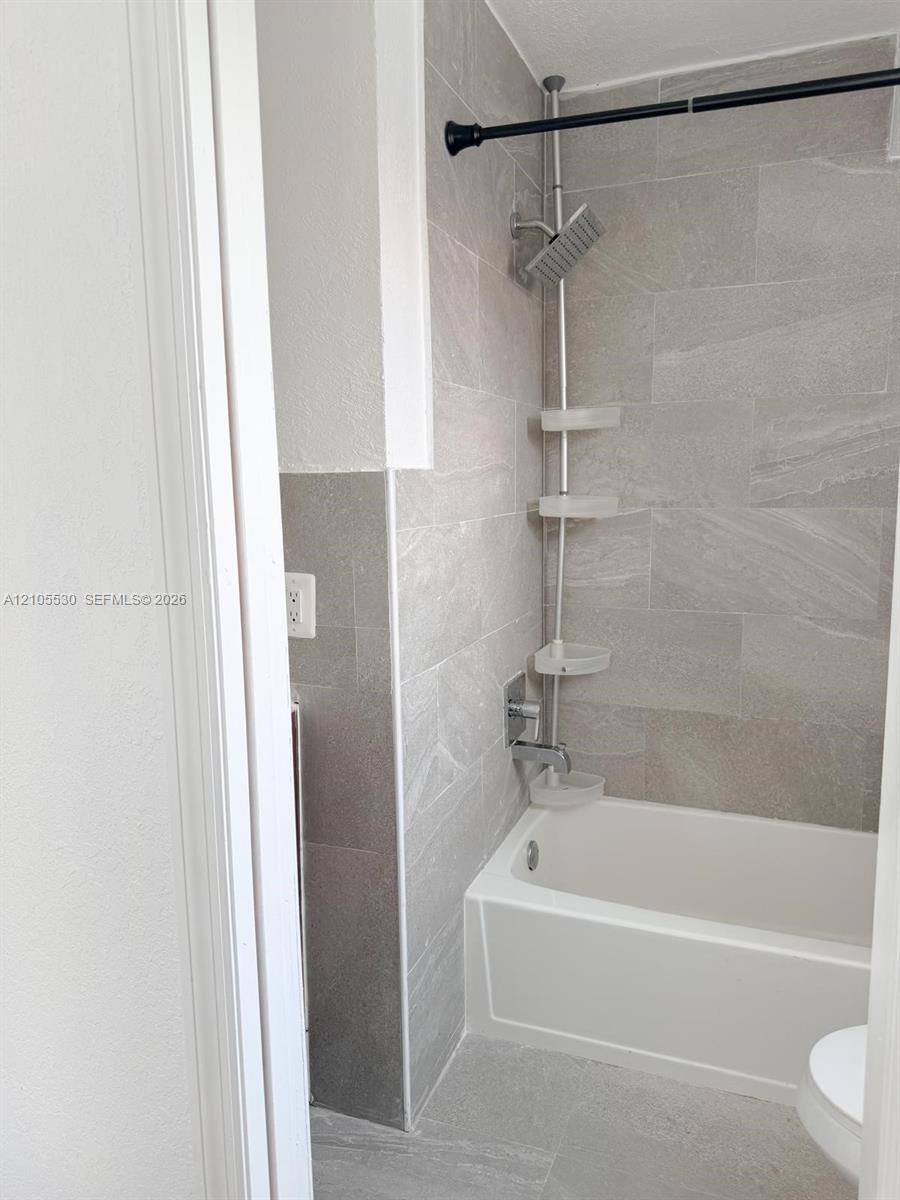 Bathtub and shower combination with light gray tiled surround and coordinating floor tiles