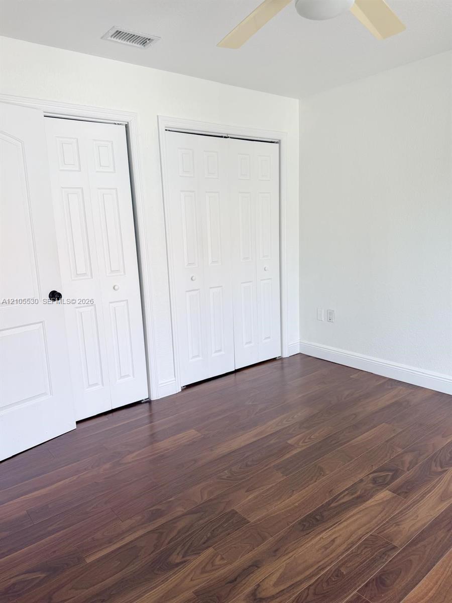 Wood-finish flooring, white walls, two panel doors, bi-fold closet doors, and a ceiling fan