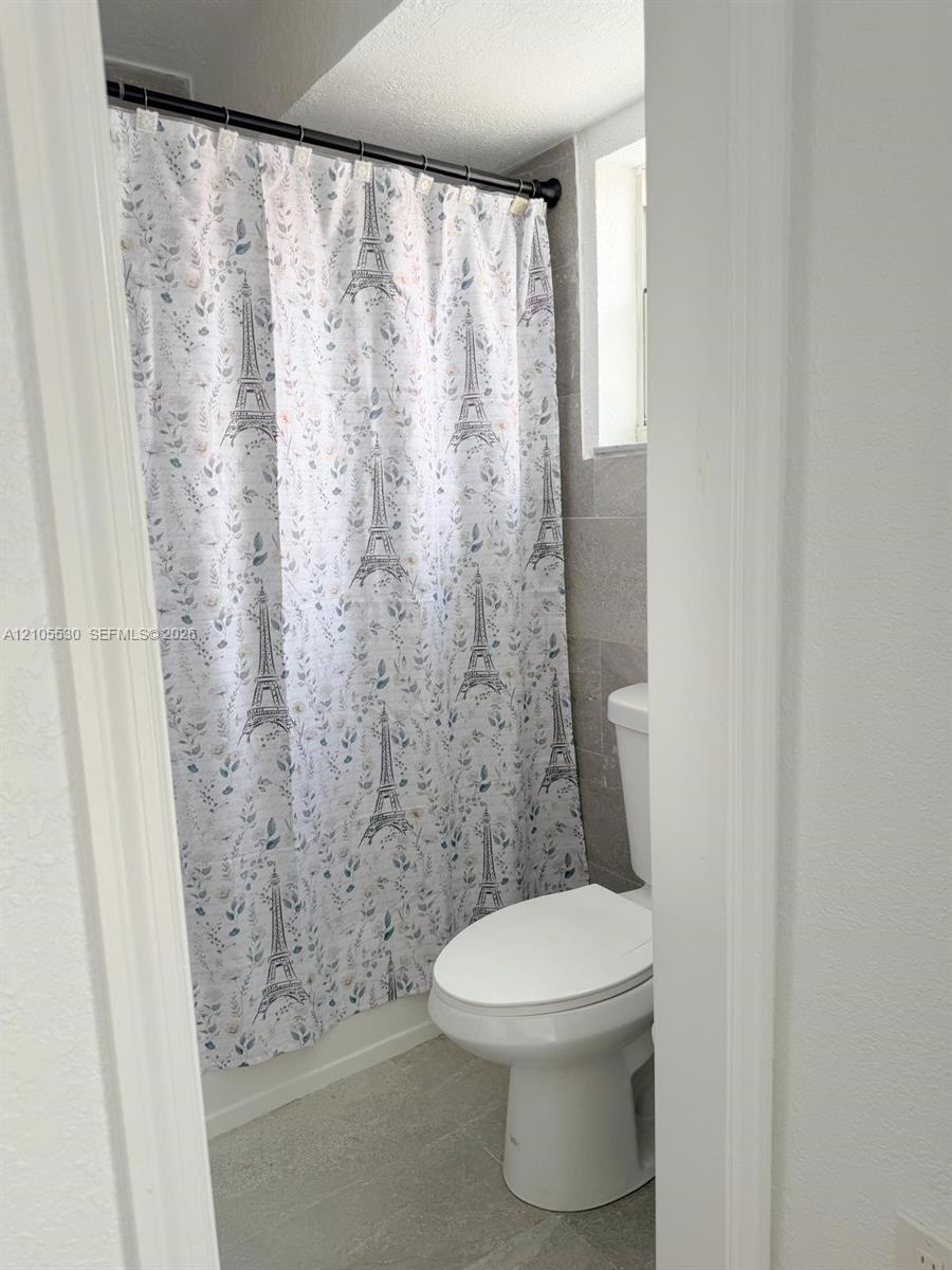 Tiled shower surround with a white toilet and light-toned flooring