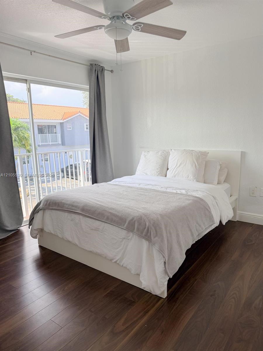 Dark wood-finish flooring, sliding glass door, overhead ceiling fan with light, white walls, and a white balcony railing
