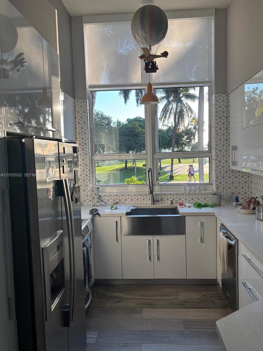 Kitchen featuring high-gloss cabinetry, stainless steel farmhouse sink, geometric tile backsplash, quartz countertops, and wood-finish flooring