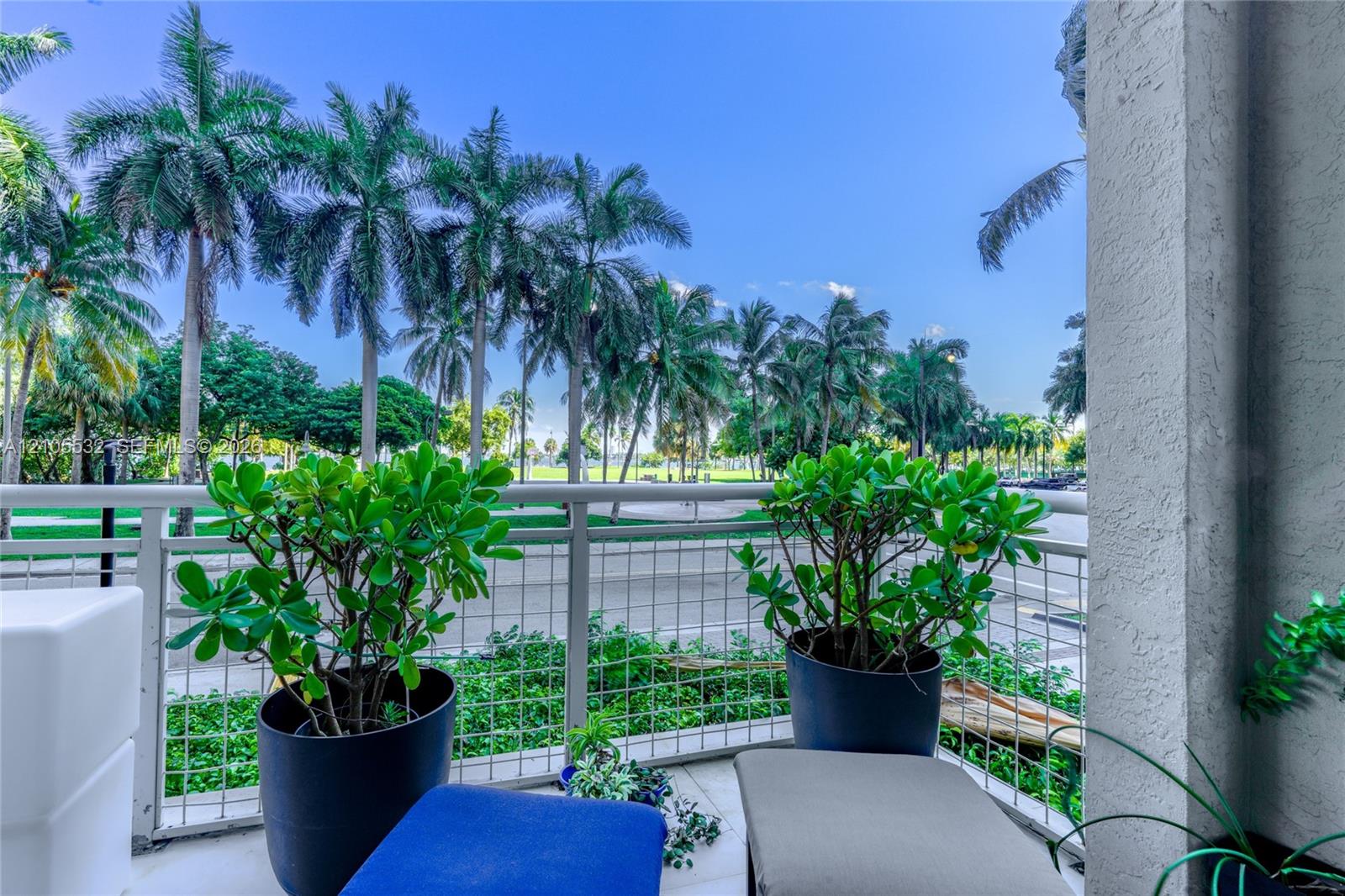 Covered balcony with white metal lattice railing, tiled flooring, and mature palm tree scenery
