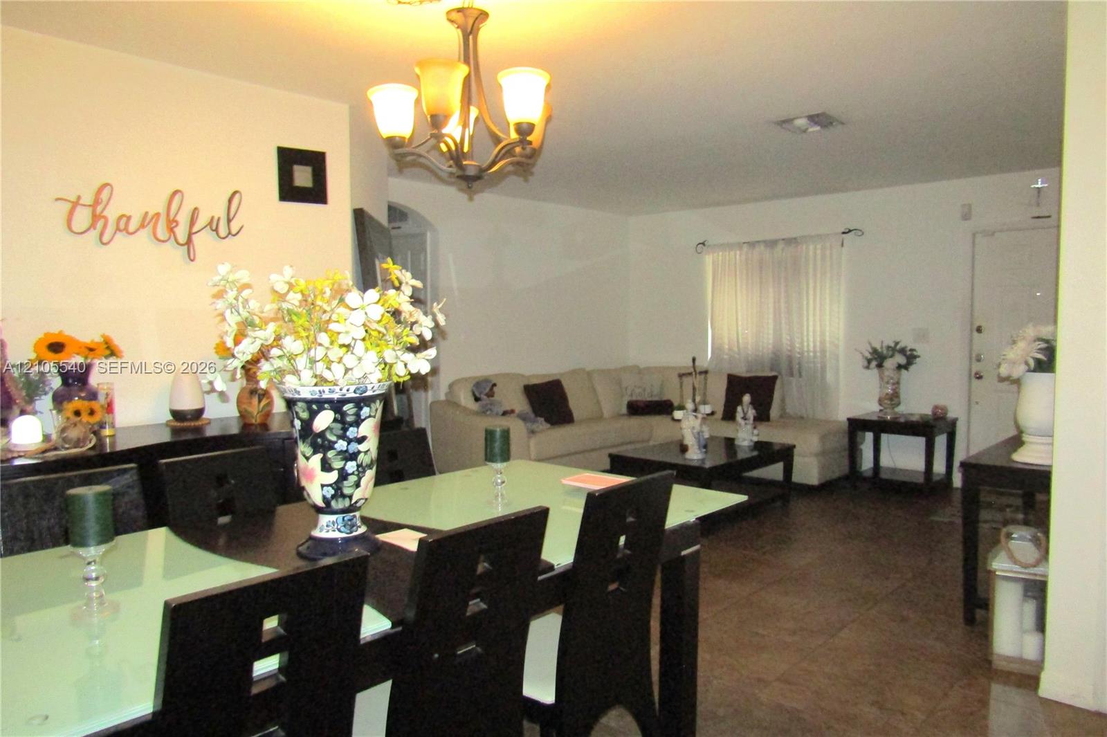 Open concept living and dining areas featuring dark wood-finish flooring, a decorative archway, and a chandelier light fixture