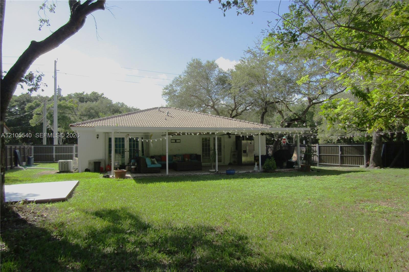 Expansive grass lawn with mature trees, a tile roof, and a covered back patio with support columns