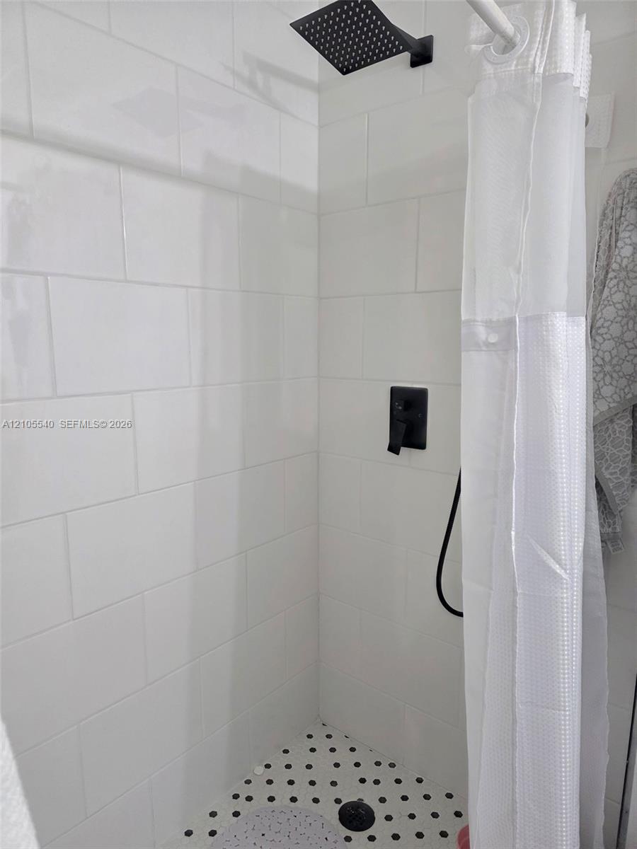 Shower with white subway tile, a matte black shower head, and a black and white mosaic tile floor