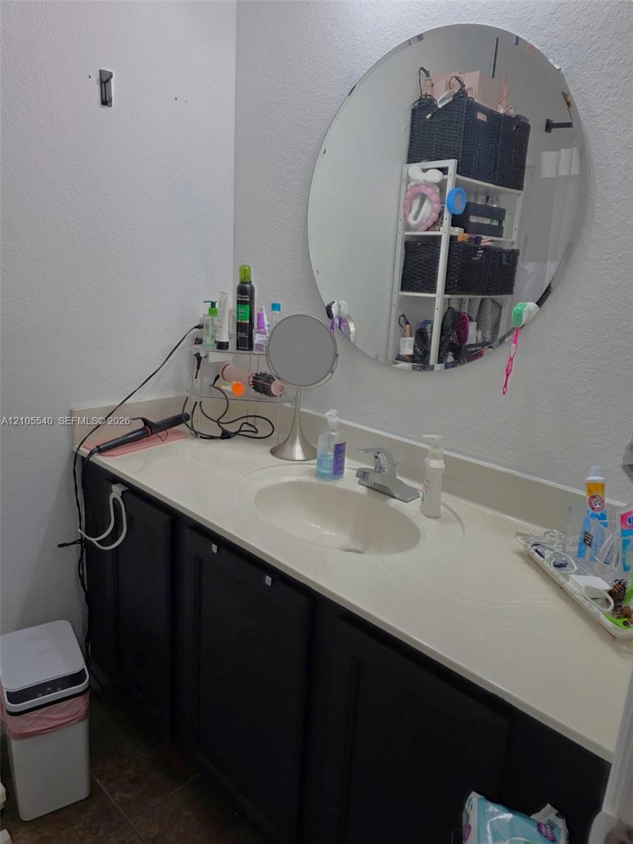 Single vanity with integrated sink, dark wood-finish cabinetry, and a circular wall-mounted mirror