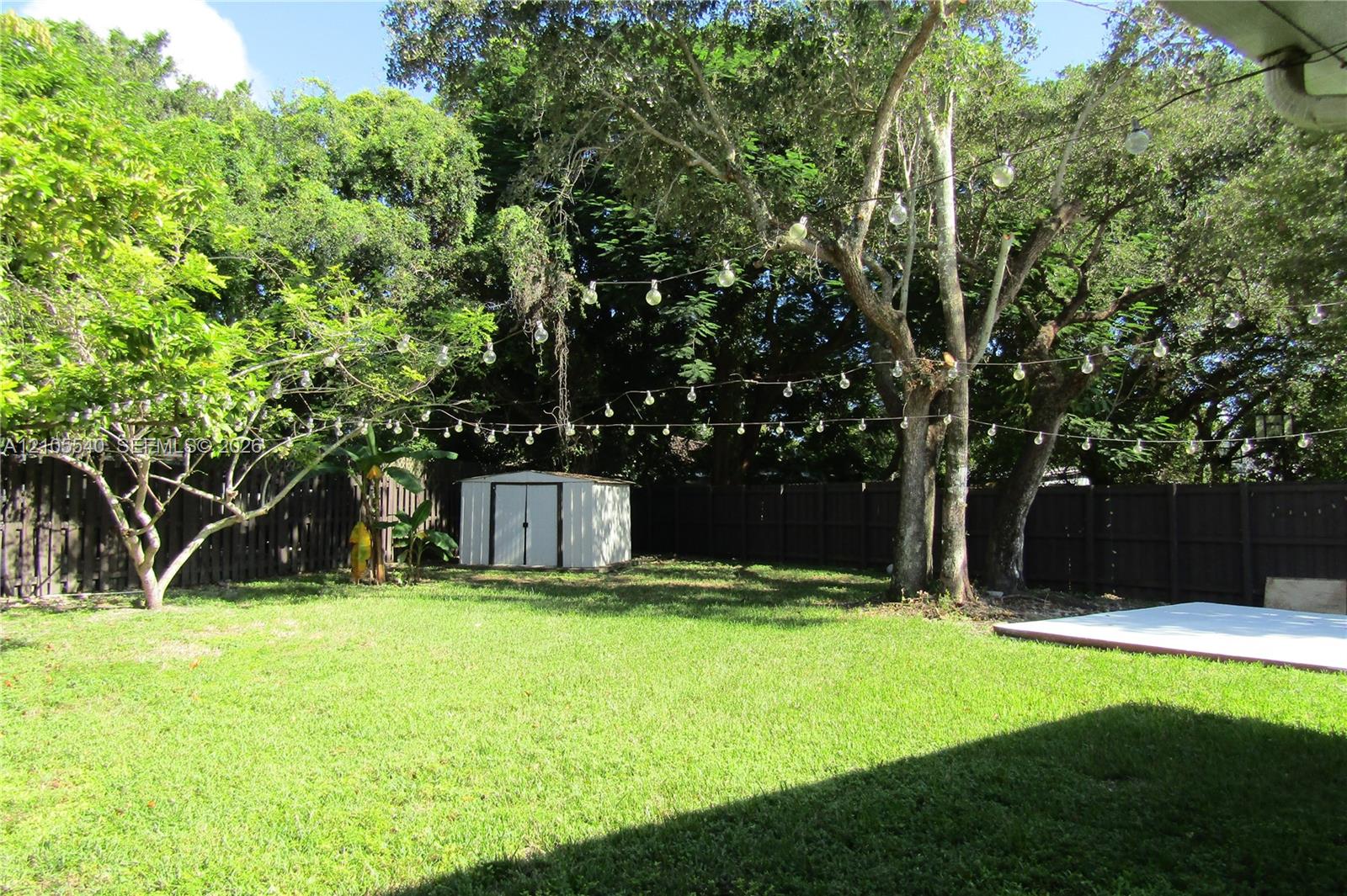 Expansive backyard featuring a lush lawn, mature trees, a privacy fence, and a storage shed