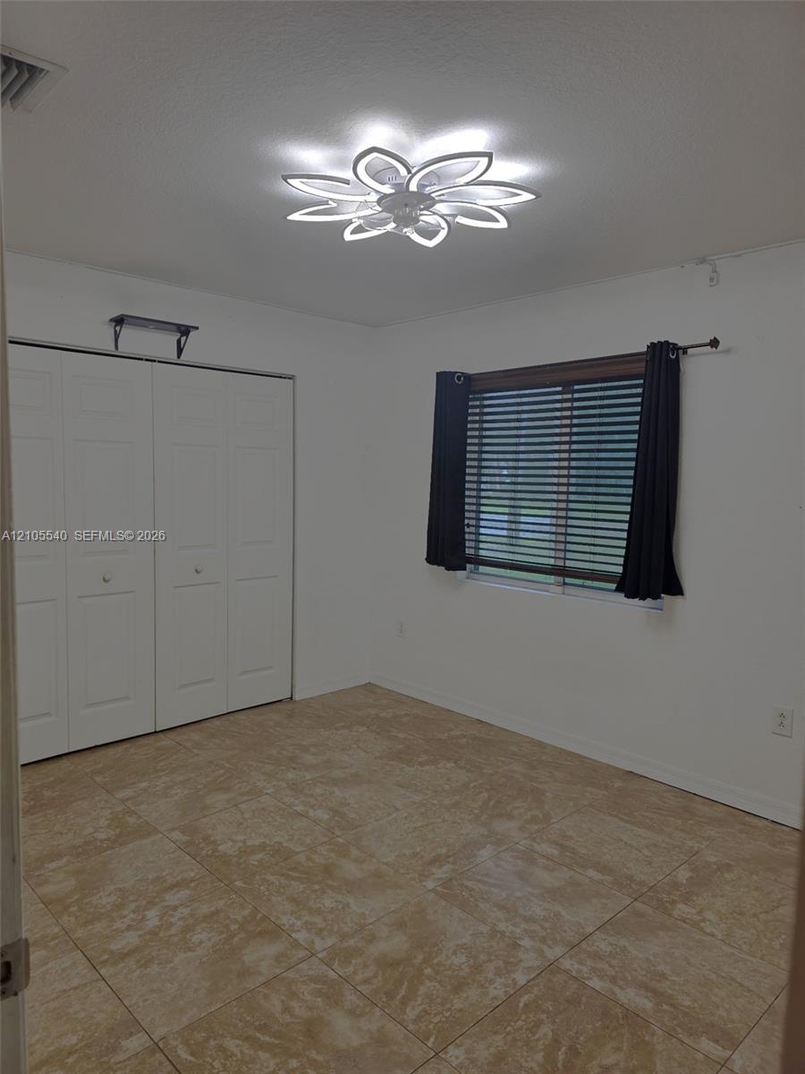 Neutral-toned tile flooring, contemporary ceiling light fixture, white bi-fold closet doors, and a window with blinds