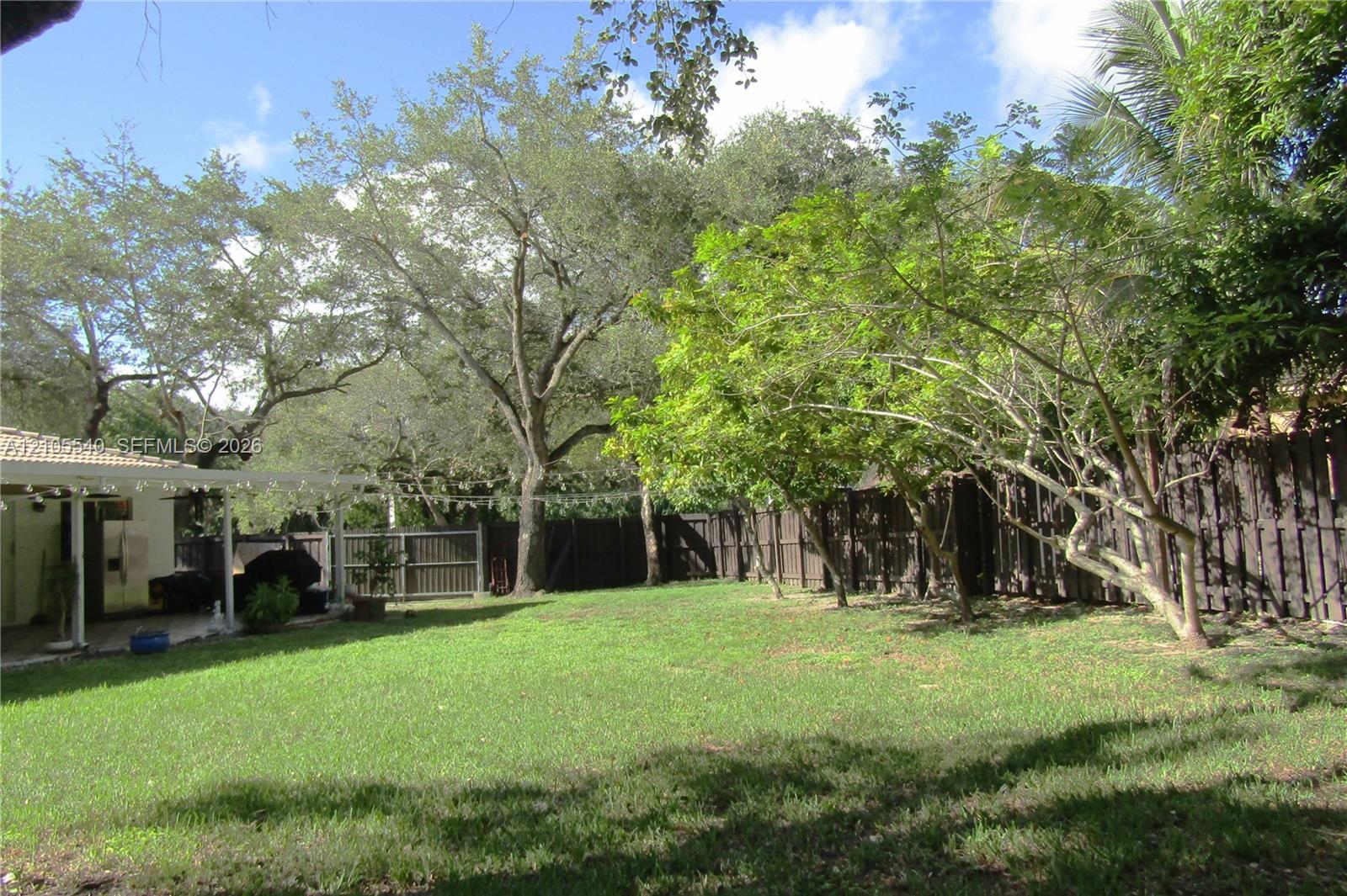 Spacious backyard featuring a manicured lawn, established trees, and a privacy fence
