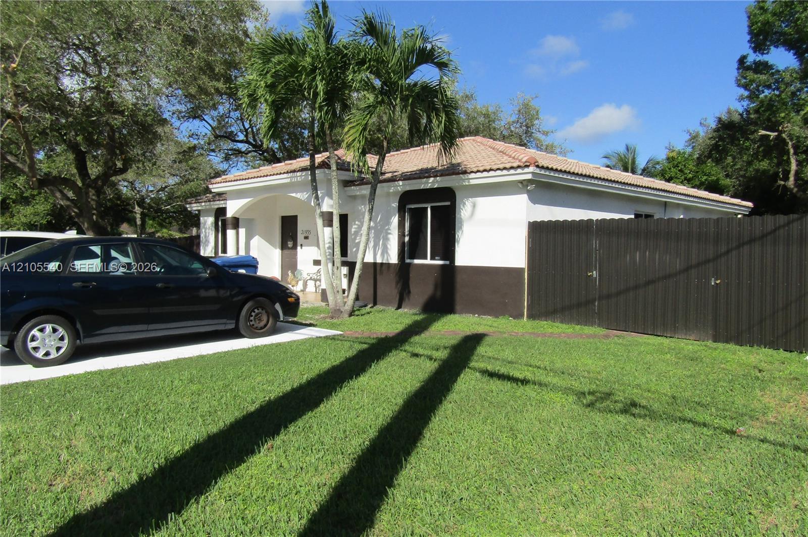 White exterior with a brown lower facade, featuring a red tile roof and a concrete driveway