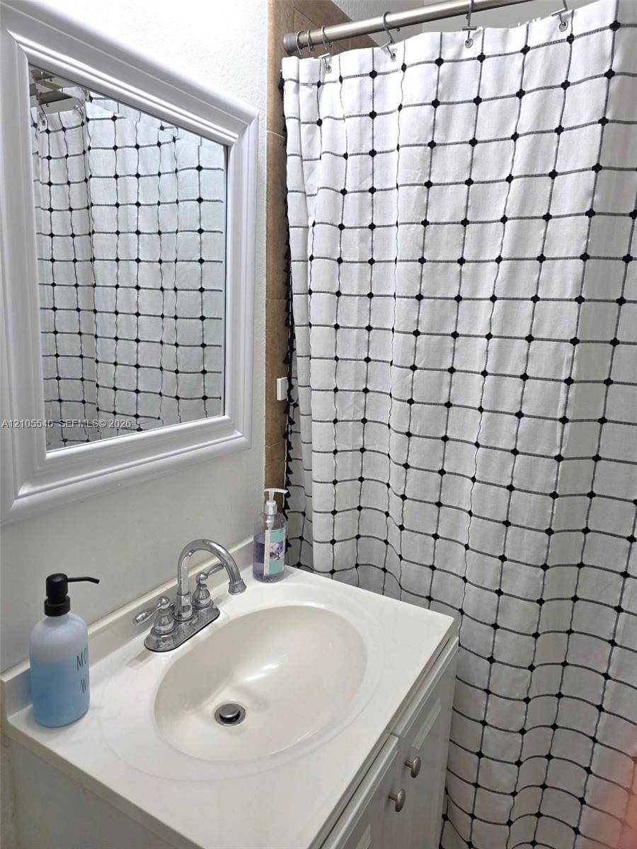 Vanity with integrated sink and chrome faucet, framed mirror, and tiled shower surround