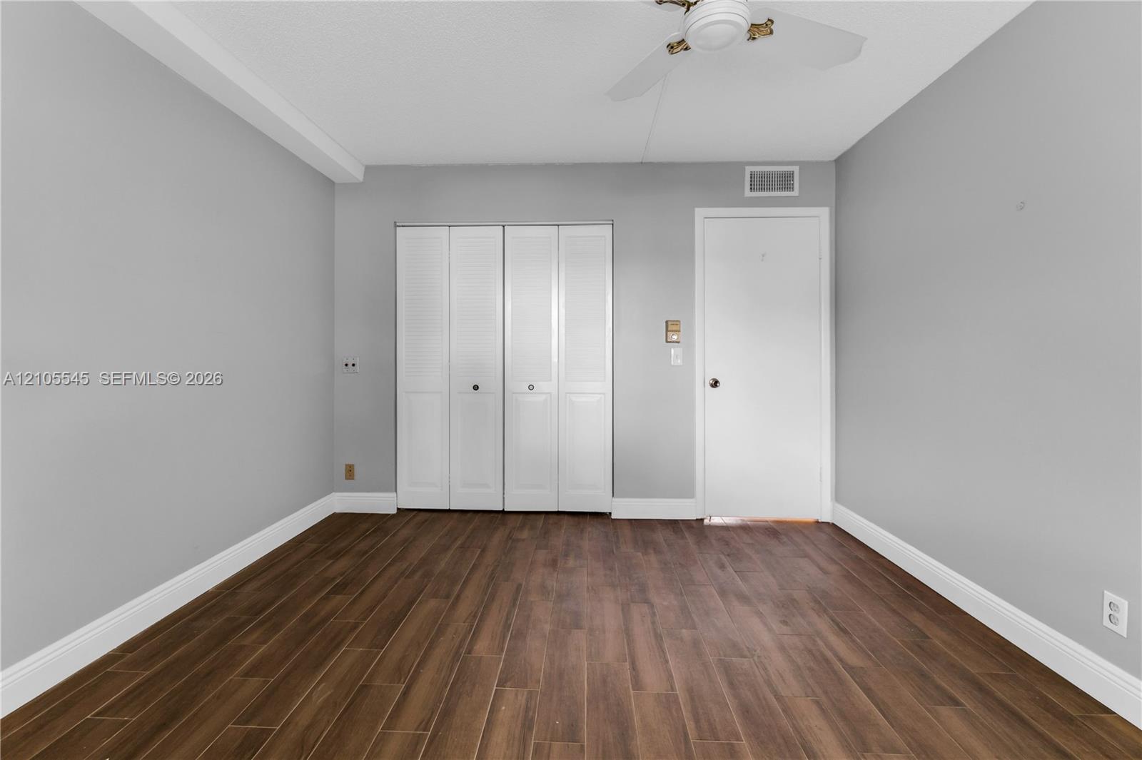 Wood-finish ceramic flooring, white bi-fold closet doors, ceiling fan, and light gray wall paint